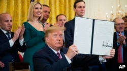 President Donald Trump holds up an executive order he signed to help combat anti-Semitism in the U. S., during a Hanukkah reception in the East Room of the White House, Dec. 11, 2019, in Washington. 