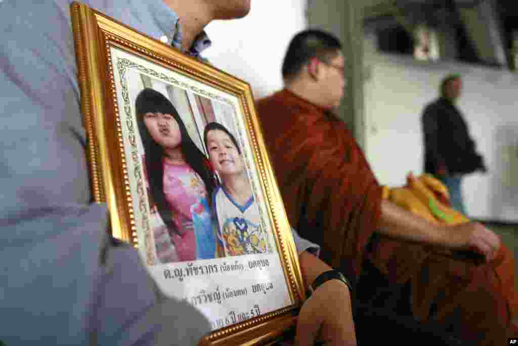 Tayakorn Yos-ubon, left, the father of two children killed in a bomb attack on Feb. 23 at an anti-government protest site, holds their portrait as he waits with a monk for their bodies at a hospital in Bangkok, Feb. 24, 2014.