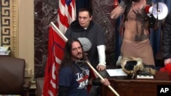 En esta imagen de archivo del video de la Policía del Capitolio, Paul Allard Hodgkins, de 38 años, de Tampa, Florida, al frente, está parado en el piso del Senado, el 6 de enero de 2021, en Washington DC.
