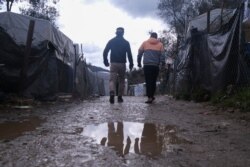 FILE - Migrants walk past makeshift tents outside the perimeter of the overcrowded Moria refugee camp on the northeastern Aegean island of Lesbos, Greece, March 11, 2020.