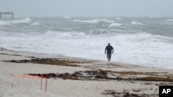A beach goer walks along the shore as waves churned up by Tropical Storm Isaias crash near Jaycee Beach Park, in Vero Beach, Florida, Aug. 2, 2020. 