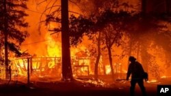 Un bombero pasa junto a una casa en llamas mientras el incendio Dixie avanza por el condado de Plumas, California, el 24 de julio de 2021.