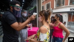 A mask-wearing shopper gets her temperature checked before entering a store in a downtown shopping district in Sao Paulo, Brazil, June 10, 2020.