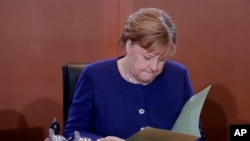 FILE - German Chancellor Angela Merkel reads documents after she arrives for the weekly Cabinet meeting of the German government at the chancellery in Berlin, Jan. 8, 2020. 