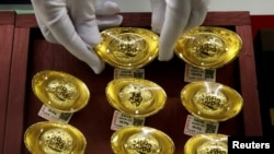 Seorang asisten toko meletakan ornamen emas di toko perhiasan Caibai Jewelry di Beijing, China, 6 Agustus 2019. (Foto: Reuters)