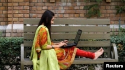 FILE - A student works on her computer sitting on a bench at Shaheed Benazir Bhutto Women's University in Peshawar, Pakistan, Oct. 19, 2017.