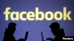FILE - Silhouettes of laptop users are seen next to a screen projection of Facebook logo in this illustration, March 28, 2018. 