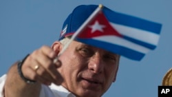 FILE - Cuba's President Miguel Diaz-Canel holds a national flag while watching the May Day parade file past at Revolution Square, in Havana, Cuba, May 1, 2018.