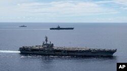 In this photo provided by U.S. Navy, the USS Ronald Reagan (CVN 76, front) and USS Nimitz (CVN 68, rear) Carrier Strike Groups sail together in formation, in the South China Sea, July 6, 2020. 