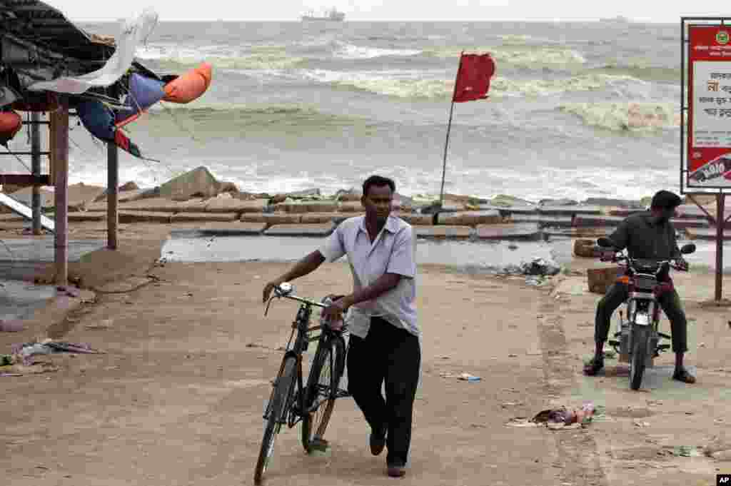 Dua warga Bangladesh melalui tanda bendera merah peringatan datangnya badai tropis Mahasen di pantai Teluk Benggala di Chittagong, Bangladesh,16 Mei 2013.