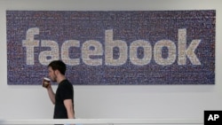 FILE - Facebook employee walks past a sign at company headquarters in Menlo Park, California.