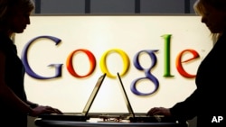 Dua pekerja sedang bekerja dengan latar logo Google di pameran industri Hannover Messe di Hannover, Jerman, 17 April 2007. (Foto: Jens Meyer/AP Photo/arsip)
