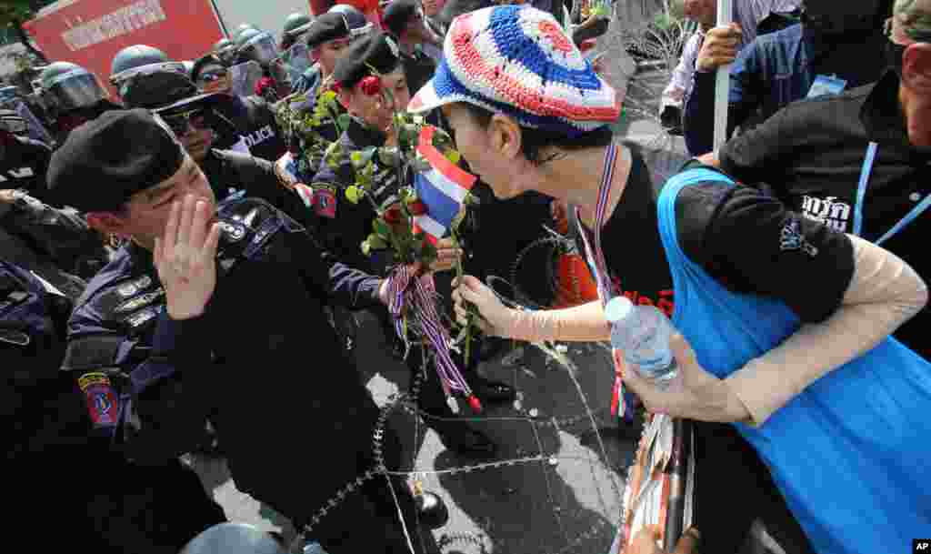 Seorang demonstran memberikan mawar pada polisi Thailand selama protes di Bangkok (25/11). Kota itu mengalami gangguan besar Senin karena protes anti-pemerintah yang masih di 13 lokasi untuk mendesak PM Yingluck Shinawatra supaya mundur. (AP/Sakchai Lalit)