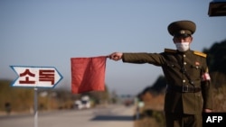 Seorang petugas ketertiban umum mengacungkan bendera merah untuk menghentikan sebuah taksi untuk dibersihkan dengan disinfektan sebagai pencegahan wabah COVID-19 jalan masuk Wonsan, Provinsi Kangwon, Korea Utara, 29 Oktober 2020.
