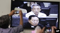 Journalists take photographs at a television screen showing the trial of Kaing Guek Eav alias Duch, former chief of the S-21 prison, at the Extraordinary Chambers in the Courts of Cambodia (ECCC) on the outskirts of Phnom Penh, February 3, 2012.