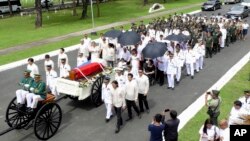 In this photo provided by the Office of Ilocos Norte Governor Imee Marcos, Imelda Marcos, in black on a wheelchair under an umbrella, the widow of the late dictator Ferdinand Marcos, and their close relatives follow the flag-draped casket of Ferdinand Mar