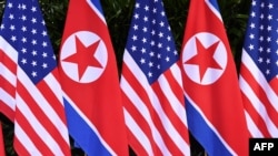 Bendera Korea Utara dan AS berdiri berdampingan di lokasi di mana pemimpin Korea Utara Kim Jong Un bertemu dengan Presiden AS Donald Trump untuk pertemuan puncak AS-Korea Utara, di Hotel Capella di Pulau Sentosa, Singapura, 12 Juni 2018. (Foto: AFP)