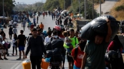 FILE - Migrants carry their belongings as they flee a road leading from Moria to the capital of Mytilene, on the northeastern island of Lesbos, Greece, Sept. 17, 2020.