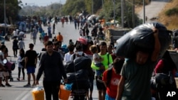 FILE - Migrants carry their belongings as they flee a road leading from Moria to the capital of Mytilene, on the northeastern island of Lesbos, Greece, Sept. 17, 2020. 