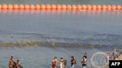 Sejumlah migran berjalan di antara kawat berduri dan pelampung di sepanjang perbatasan antara AS-Meksiko di sungai Rio Grande di Eagle Pass, Texas, pada 16 Juli 2023. (Foto: AFP/Suzanne Cordeiro)