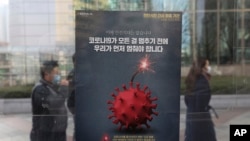 Orang-orang yang mengenakan masker sebagai tindakan pencegahan terhadap virus corona melewati poster yang menekankan kampanye jarak sosial yang ditingkatkan di sebuah stasiun bus di Seoul, Korea Selatan, Senin, 7 Desember 2020. (Foto: AP)