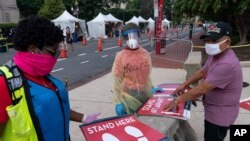 Trabalhadores do Departamento de Saúde em Washington, D.C. preparam sinais na F Street sobre locais de testagem para a Covi-19. 14 Ago., 2020