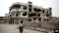 Seorang perempuan berjalan melewati bagian yang hancur di kota Homs, Suriah (5/6). (AP/Dusan Vranic)