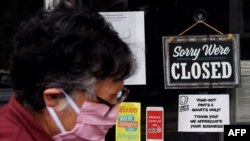 Seorang perempuan mengenakan masker berjalan melewati tanda di jendela toko makanan yang tutup selama pandemi Covid-19 di Arlington, Virgina, 4 Mei 2020. (Foto: dok).