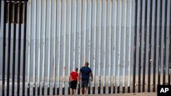 Two people walk towards metal bars marking the United States border where it meets the Pacific Ocean, March 2, 2016, in Tijuana, Mexico. 